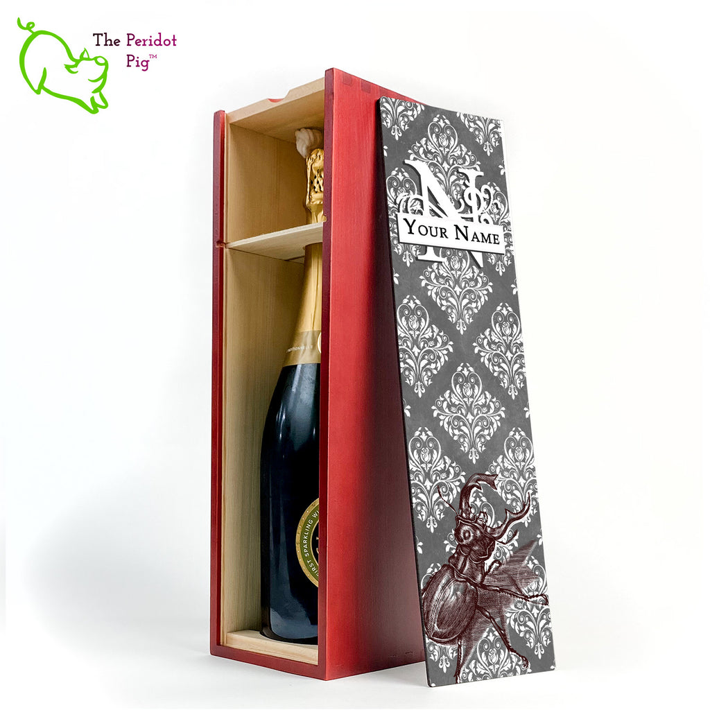 The wine box front panel is decorated in a glossy, detailed print with a white monogram and space for a customized name. This model has a gray background with white decorative scroll work. In the foreground is a large burgundy line drawing of a rhinoceros beetle. Cherry version with the interior shown and a sample wine bottle.