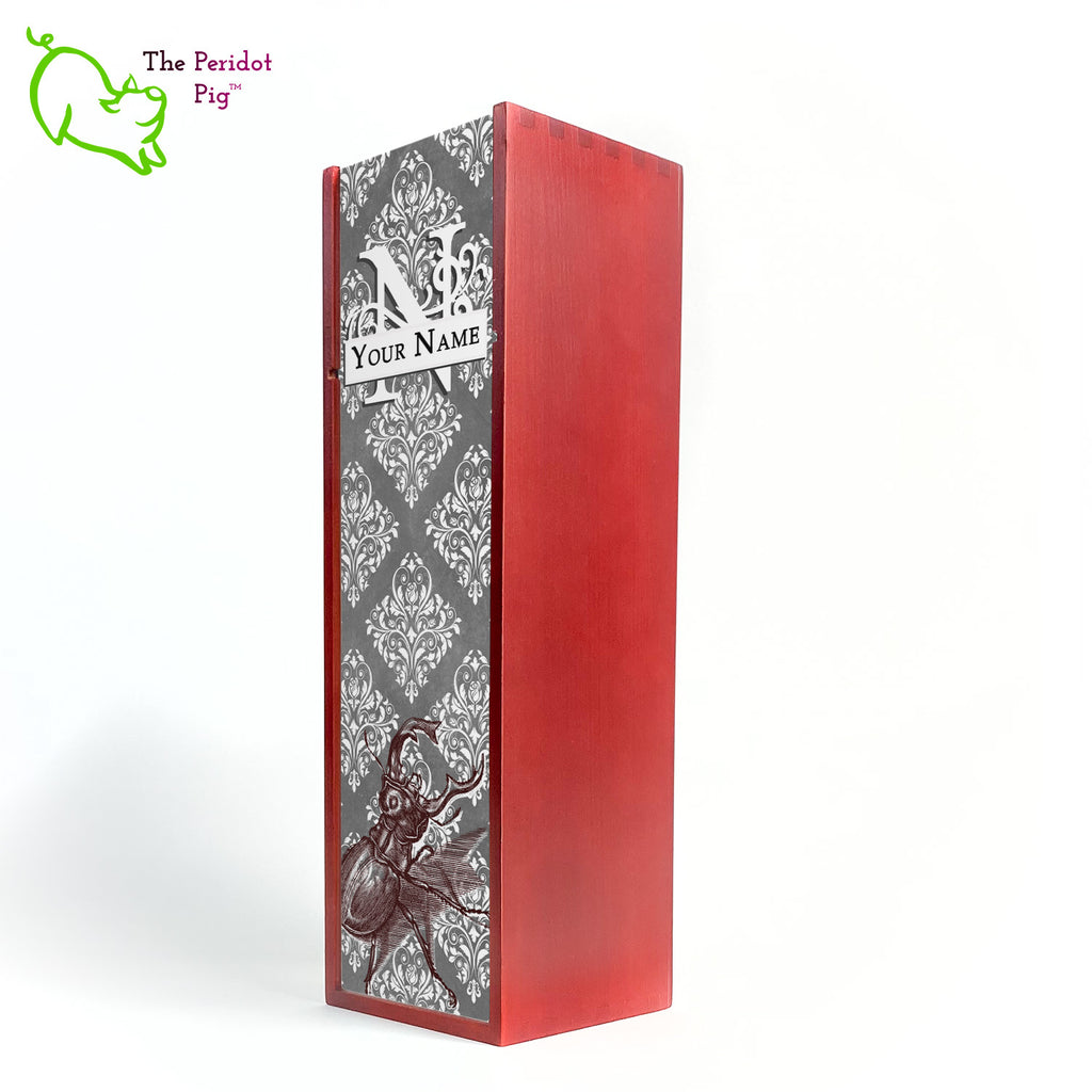 The wine box front panel is decorated in a glossy, detailed print with a white monogram and space for a customized name. This model has a gray background with white decorative scroll work. In the foreground is a large burgundy line drawing of a rhinoceros beetle. Cherry version front view.