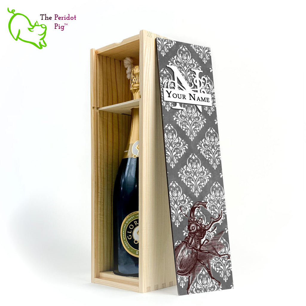 The wine box front panel is decorated in a glossy, detailed print with a white monogram and space for a customized name. This model has a gray background with white decorative scroll work. In the foreground is a large burgundy line drawing of a rhinoceros beetle. Natural version with the interior shown and a sample wine bottle.