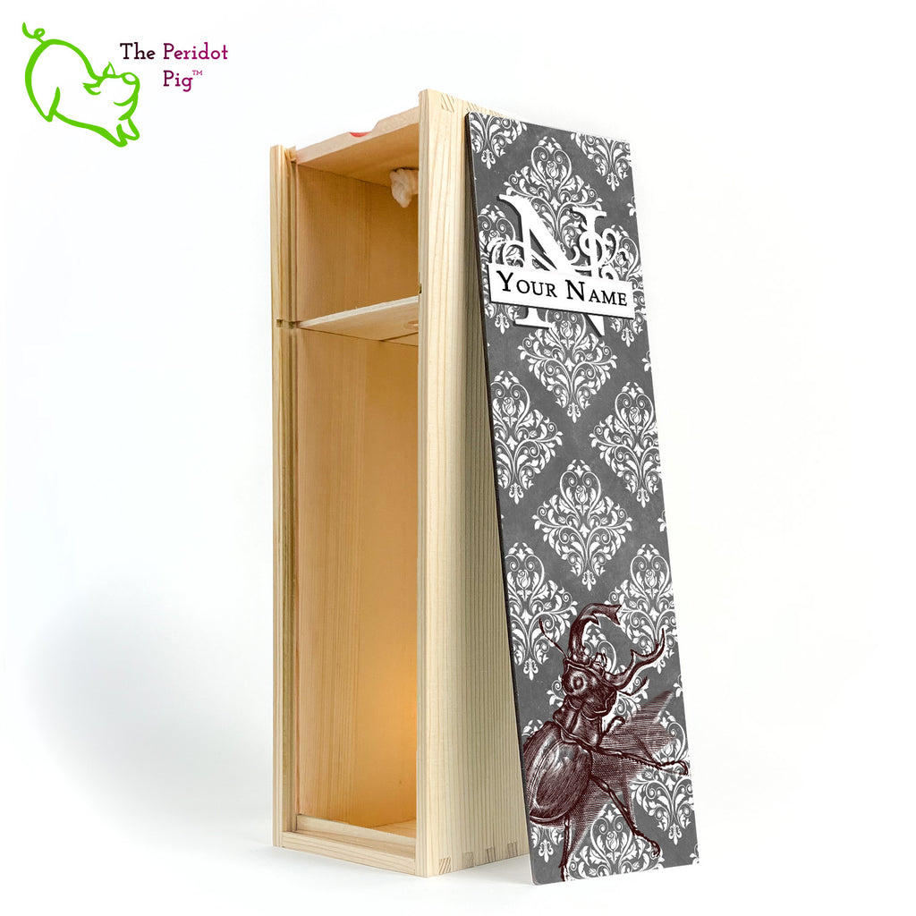 The wine box front panel is decorated in a glossy, detailed print with a white monogram and space for a customized name. This model has a gray background with white decorative scroll work. In the foreground is a large burgundy line drawing of a rhinoceros beetle. Natural version with the interior shown.