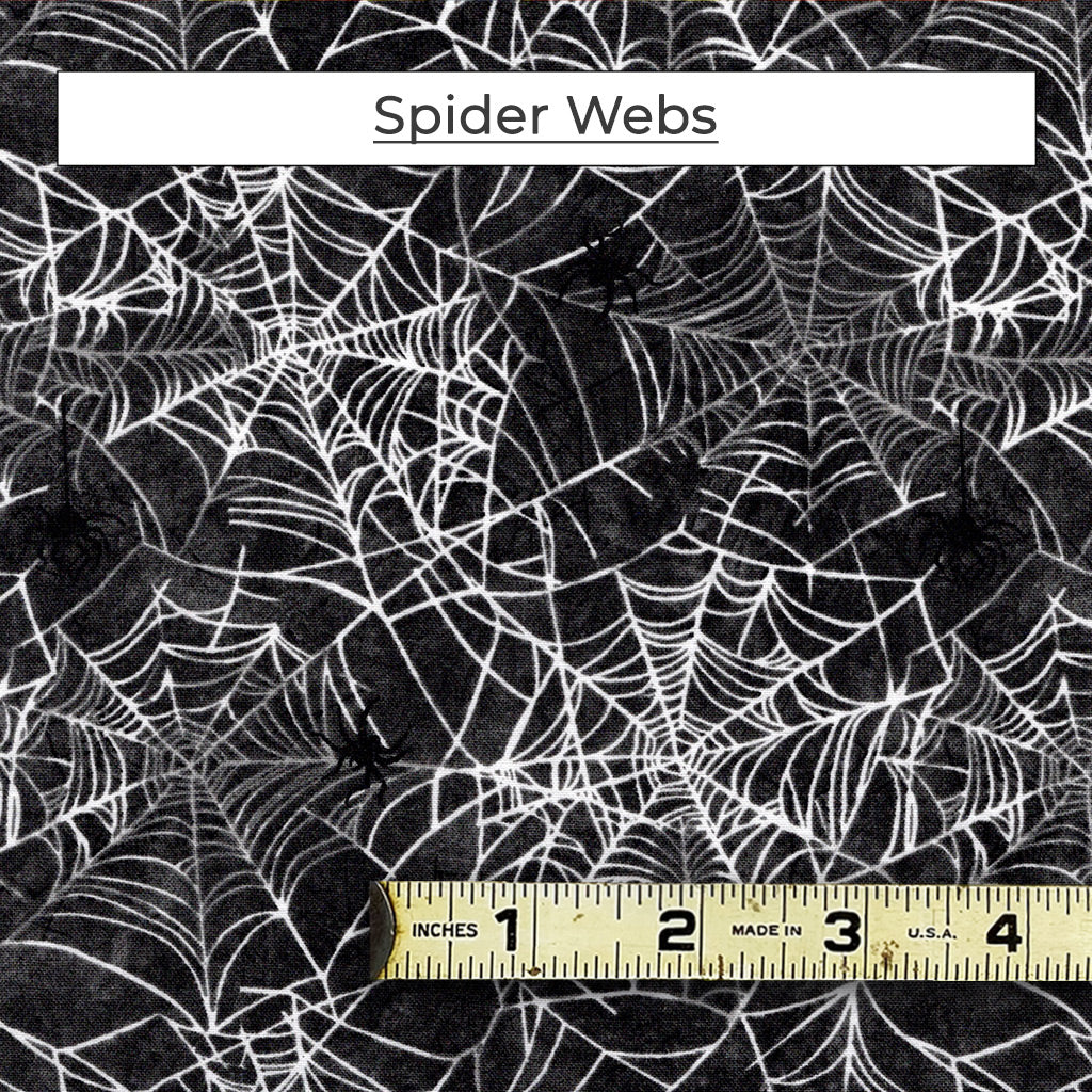 The Spider Webs fabric is a mix of white and grey spider webs on a black background. There are little black spiders dangling from the webs. 