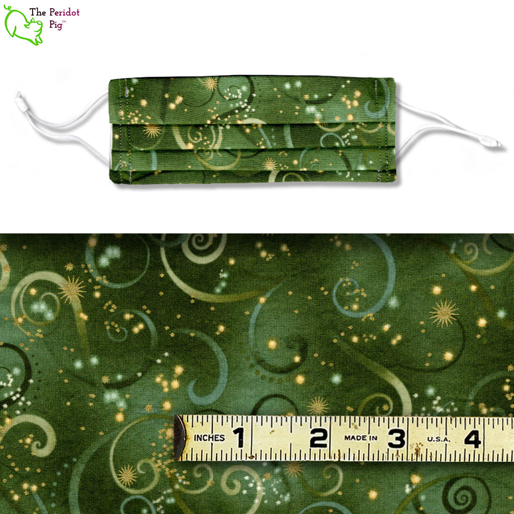 A green fabric with swoops and swirls in different shades of green and gold. Called Firefly Dance, shown with ruler.