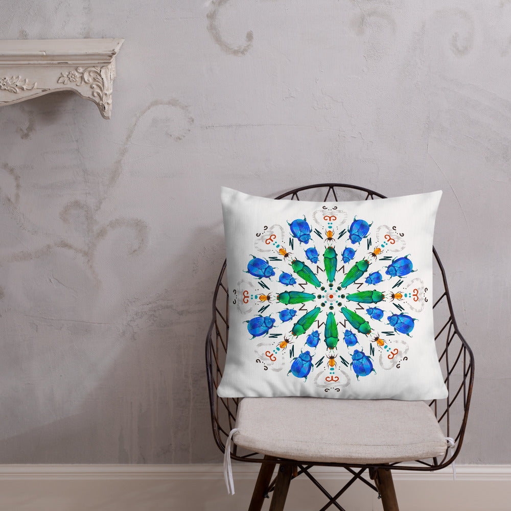 A colorful mandala of beetles graces this white pillow and is availble in either 18"x18" or 22"x22" sizes. The image is printed on both the front and back. The center beetles have shades of bright green. The smaller beetles are blue and orange. 22" front view shown on a chair.