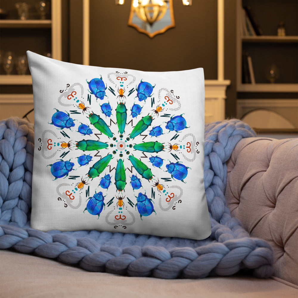 A colorful mandala of beetles graces this white pillow and is availble in either 18"x18" or 22"x22" sizes. The image is printed on both the front and back. The center beetles have shades of bright green. The smaller beetles are blue and orange. 22" front view shown on a couch.