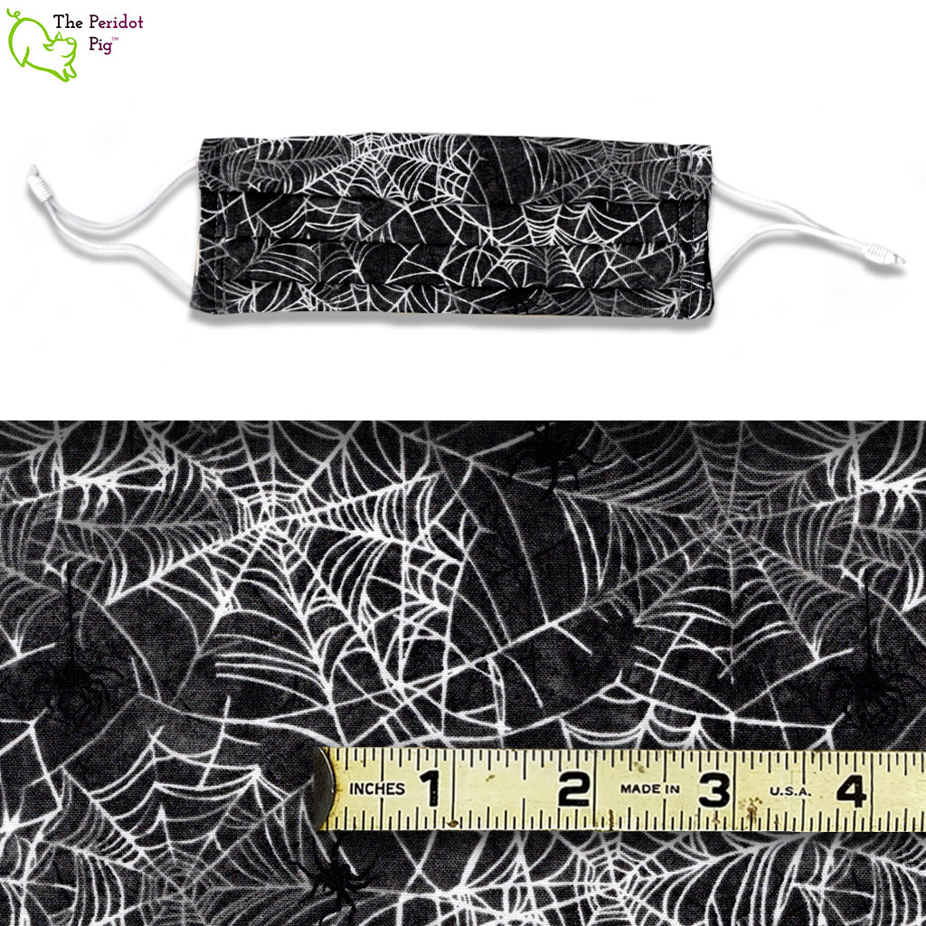 Image showing mask and fabric swatch. The Spider Webs fabric is a mix of white and grey spider webs on a black background. There are little black spiders dangling from the webs. 